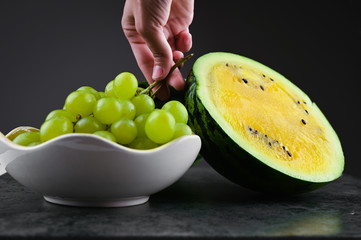 yellow watermelon with grapes. on a dark background