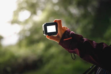 Hand holding action camera with white display screen.