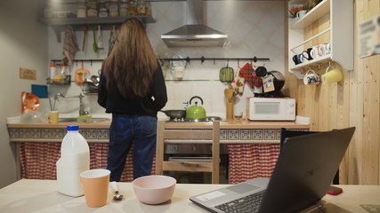 Young woman working laptop computer and eats Corn Flakes Cereal at home kitchen.