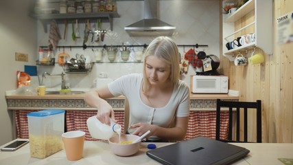 Young woman working laptop computer and eats Corn Flakes Cereal at home kitchen.