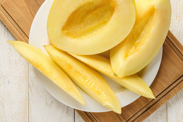 Ripe juicy honeydew melon halves and slices on a white plate over wood table. Sweet fruits and berries. Vegetarian, raw food diet and healthy eating.