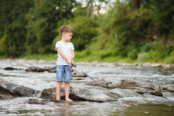 cute boy in white T shirt fishing in the river and has fun, smiles. vacation with kids, holidays, active weekends concept