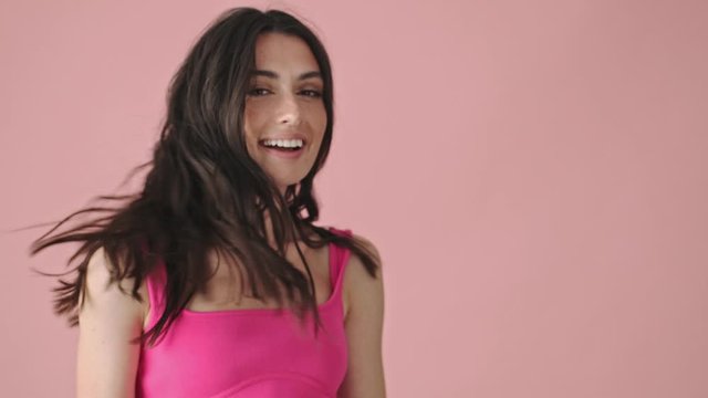 A smiling young woman is shaking her hair isolated over a pink background