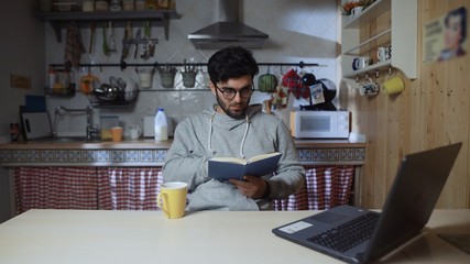 Young man reading a book in kitchen at home at night