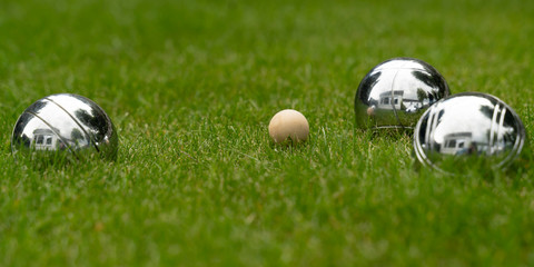 Boccia balls made of chromed steel lie on a grass surface. Play for your own garden.