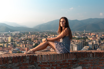 Fototapeta na wymiar Beautiful girl on the roof terrace with aerial view of the old Italian city Brescia at sunset.