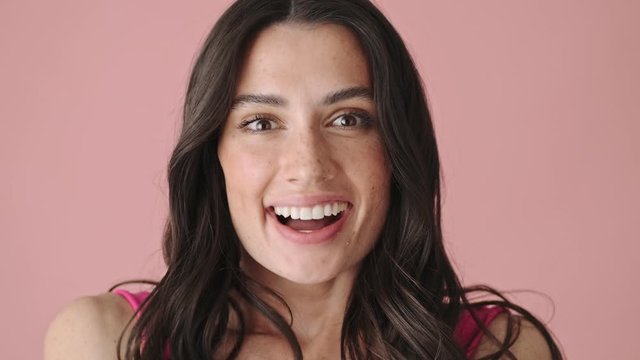 A close-up view of a surprised young woman is looking to the camera isolated over pink background