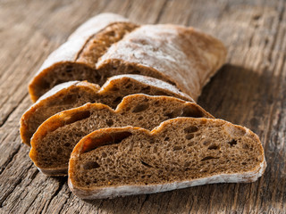Ciabatta. Dark fresh healthy flattish open-textured Italian bread with a floury crust made with olive oil on wooden background. Close-up
