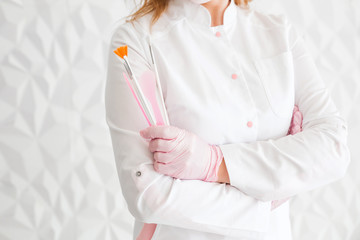 Professional beautician with brushes in hands. Woman beautician posing against white wall background