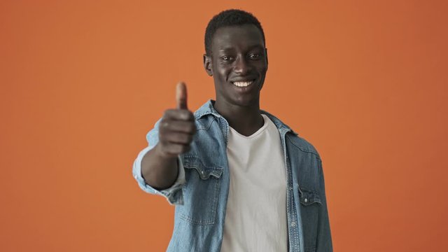 A smiling african american young man is showing thumb-up gesture isolated over orange background