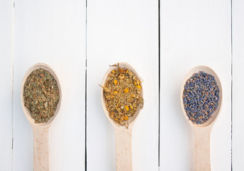 three wooden spoons with dried flowers and herbs lie in a row on a white wooden background