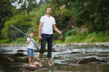 A father teaching his son how to fish on a river outside in summer sunshine