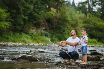 A father teaching his son how to fish on a river outside in summer sunshine