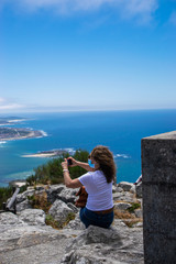 Photo of a young and attractive woman taking a photo with his phone of the estuary of the Minho river in Galicia, north of Spain wearing face mask