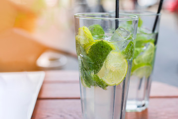 Two glasses fresh non-alcoholic cooling cocktail in summer on the terrace of a cafe. A refreshing mojito with ice, mint and lime best idea to cool off in hot summer. Vertical, selective focus