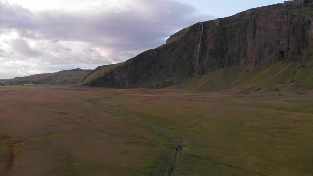 Panning aerial images that reveal a cliff full of beautiful waterfalls and surrounded by green meadows. Typical Icelandic landscape.