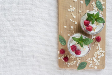 Obraz na płótnie Canvas Two portions of homemade natural yogurt with oats and fresh raspberries in glass jars on a light background. Top view, copyspase
