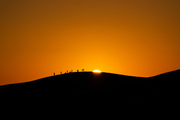 panorama dell'alba nel deserto marocchino di merzouga, con persone sullo sfondo stagliate contro il...