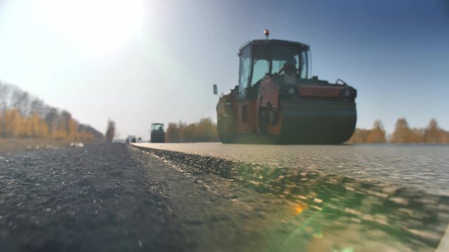 Shooting a layer of freshly laid asphalt. Road surface repair. Construction of a new road. The rollers levels and compacts the asphalt. Road rollers. Sun glare.