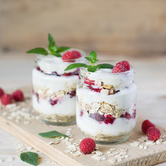 Two portions of homemade natural yogurt with oats and fresh raspberries in glass jars on a light wooden background. Selective focus. Concept of healthy breakfast.