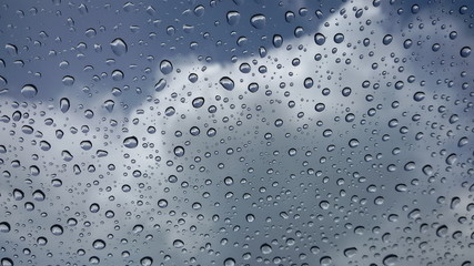Rain drops on the windshield On the sky background there are gray white clouds. Focus close and choose the subject.