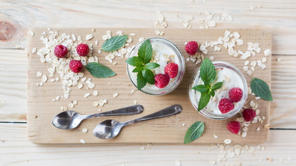 Two portions of homemade natural yogurt with oats and fresh raspberries in glass jars on a light wooden background. Selective focus. Concept of healthy breakfast.