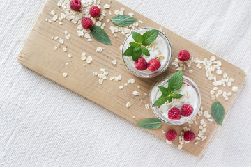 Two portions of homemade natural yogurt with oats and fresh raspberries in glass jars on a light background. Selective focus. Concept of healthy breakfast.