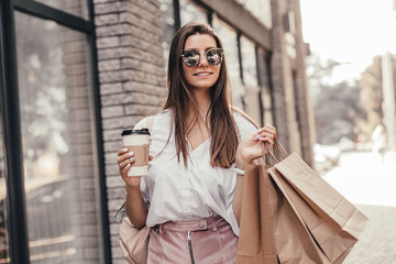 Beautiful fashionable woman drink coffee walking near mall with shopping bags.