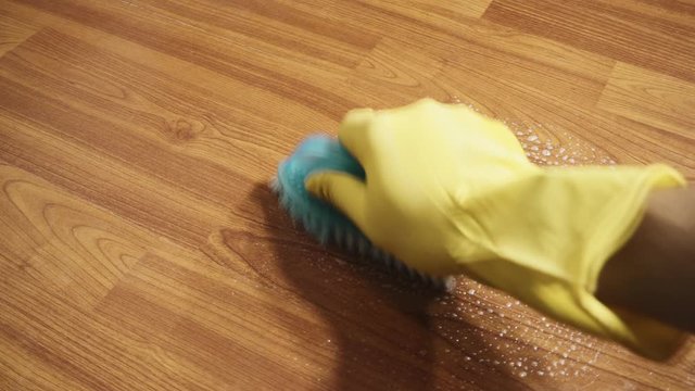 Footage of hand with yellow glove cleaning dirty parquet