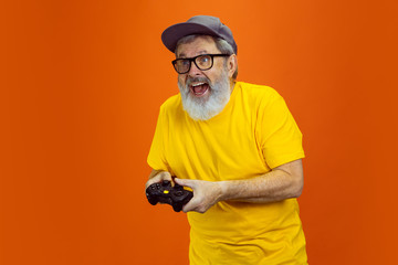 Gamer man. Portrait of senior hipster man using devices, gadgets isolated on orange studio...