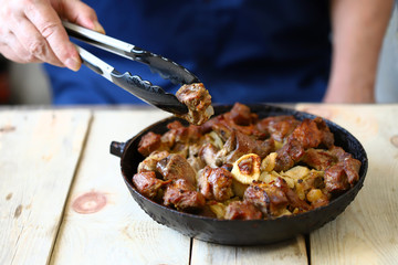 Selective focus. The chef mixes pieces of fried meat in a frying pan. Pork skewers in a skillet.