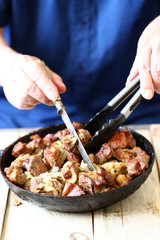 Selective focus. The chef mixes pieces of fried meat in a frying pan. Pork skewers in a skillet.