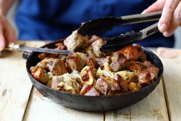 Selective focus. The chef mixes pieces of fried meat in a frying pan. Pork skewers in a skillet.