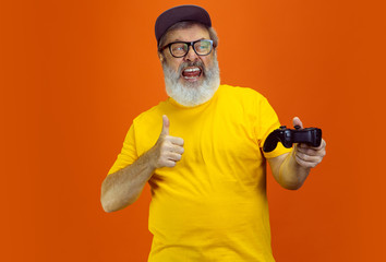 Gamer man. Portrait of senior hipster man using devices, gadgets isolated on orange studio...