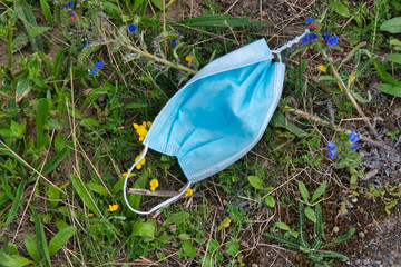 A used, blue surgical mask used for COVID-19 protection, discarded as litter in rural countryside causing environmental pollution