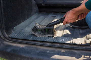 Male hands are cleaning trunk and car interior. Car care in autumn. Step-by-step dust cleaning dirty car with a dry brush.