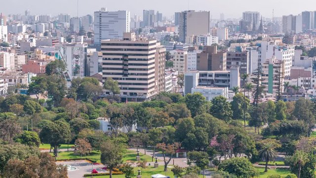 Aerial view to Park of the Reserve with magic water circuit biggest fountain complex timelapse. Green lawn and trees. City skyline on a background