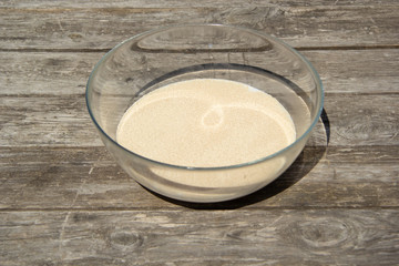 Glass bowl with milk on a wooden table. On top of milk poured dry yeast to prepare yeast dough on pizza, buns or pies