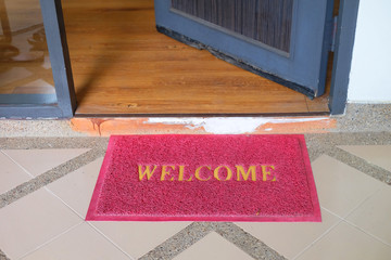 Red welcome doormat in front of opening door