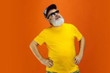 Stunning posing. Portrait of senior hipster man in eyewear isolated on orange studio background....