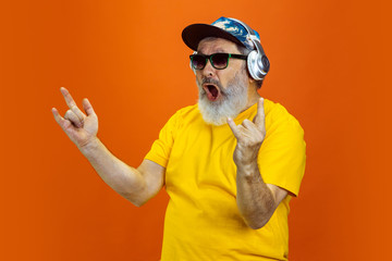 Crazy dance. Portrait of senior hipster man using devices, gadgets isolated on orange studio...