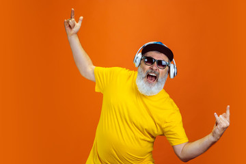 Crazy dance. Portrait of senior hipster man using devices, gadgets isolated on orange studio...