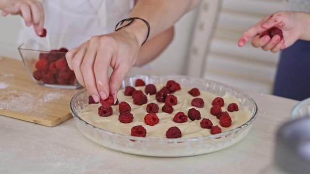 Close-up of childs with mom adding raspberry to dough. Mother with little son and daughter cooking raspberry pie. 4K, UHD