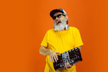 DJ-set. Portrait of senior hipster man using devices, gadgets isolated on orange studio background. Tech and joyful elderly lifestyle concept. Trendy colors, forever youth. Copyspace for your ad.