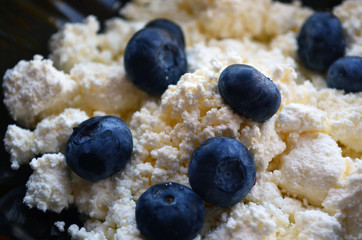 Cottage cheese with blueberries in a dark plate close-up. Breakfast.
