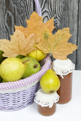 Ripe pears of the new harvest in a wicker basket. On boards painted white. Jam in jars, dried maple leaves.
