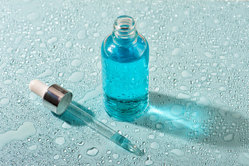 Moisturizing beauty essence in a dropper glass bottle on blue background with water drops. Spa bathroom concept, copy space for your text