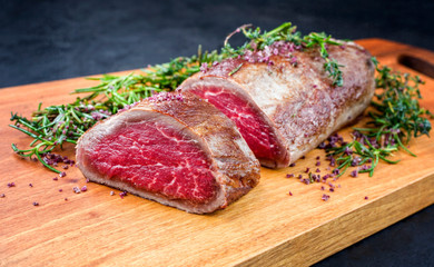 Gebratenes dry aged Angus Filet Steak vom Rind  natur mit Kräuter und Rotwein Salz angeboten als close-up auf einem Modern Design Holz Board