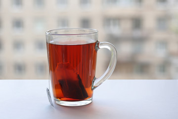 a glass mug of black tea stands on a white windowsill