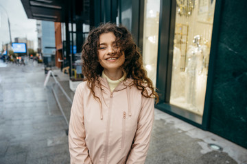 Obraz premium Charming young curly woman with beautiful smiling, walking the street of the city and turns around at rainy day